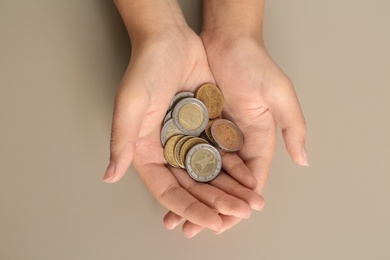 Young woman with handful of coins on beige background, top view