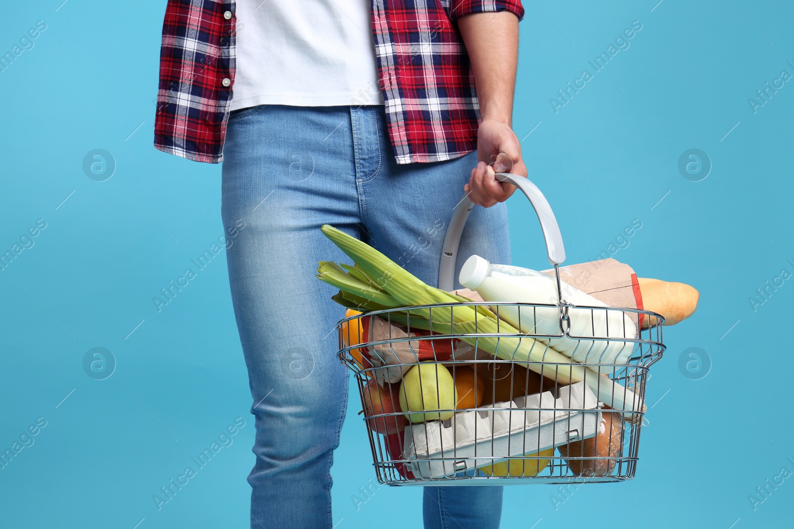 Photo of Man with shopping basket full of products on blue background, closeup