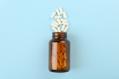 Bottle and vitamin capsules on light blue background, top view