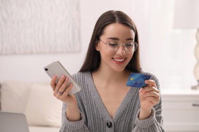 Photo of Woman with credit card using smartphone for online shopping indoors