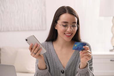 Woman with credit card using smartphone for online shopping indoors