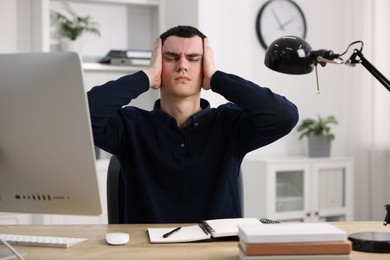 Photo of Young man suffering from headache at workplace in office