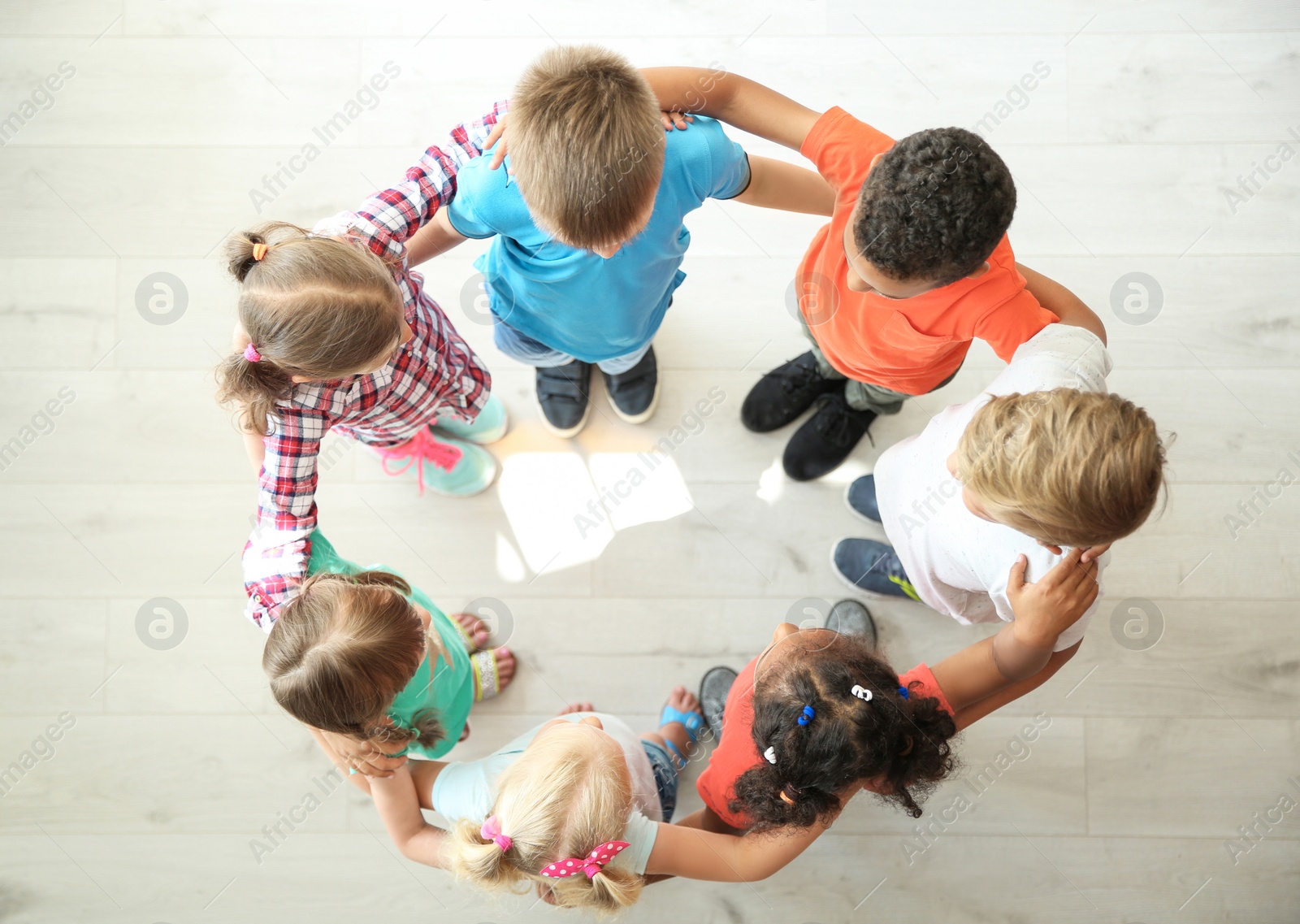 Photo of Little children making circle with hands around each other indoors, top view. Unity concept