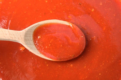 Photo of Wooden spoon above tasty tomato sauce, top view