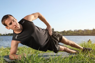 Photo of Sporty man doing side plank exercise on green grass near river