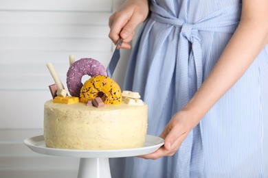 Photo of Woman cutting delicious cake decorated with sweets indoors, closeup