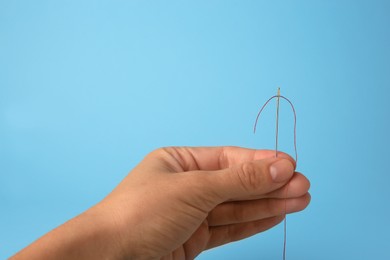 Photo of Woman holding sewing needle with thread on light blue background, closeup