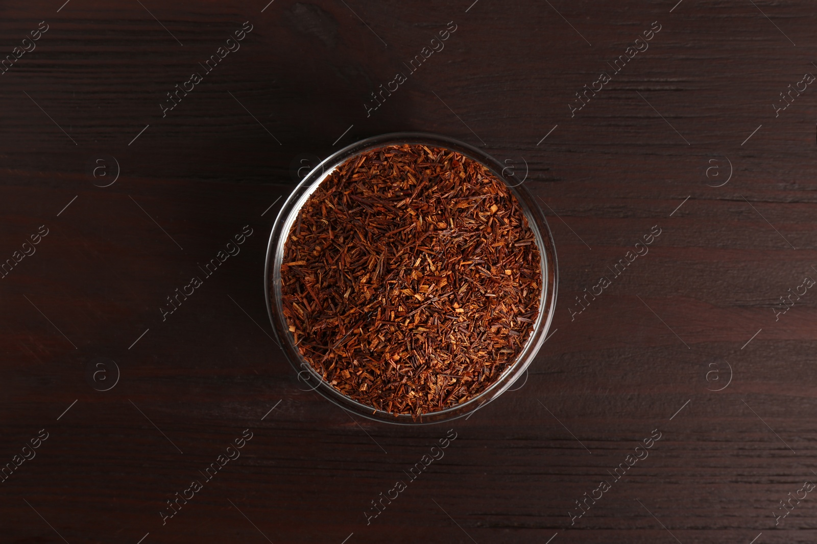 Photo of Dry rooibos leaves in glass bowl on wooden table, top view