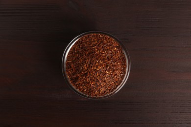 Dry rooibos leaves in glass bowl on wooden table, top view