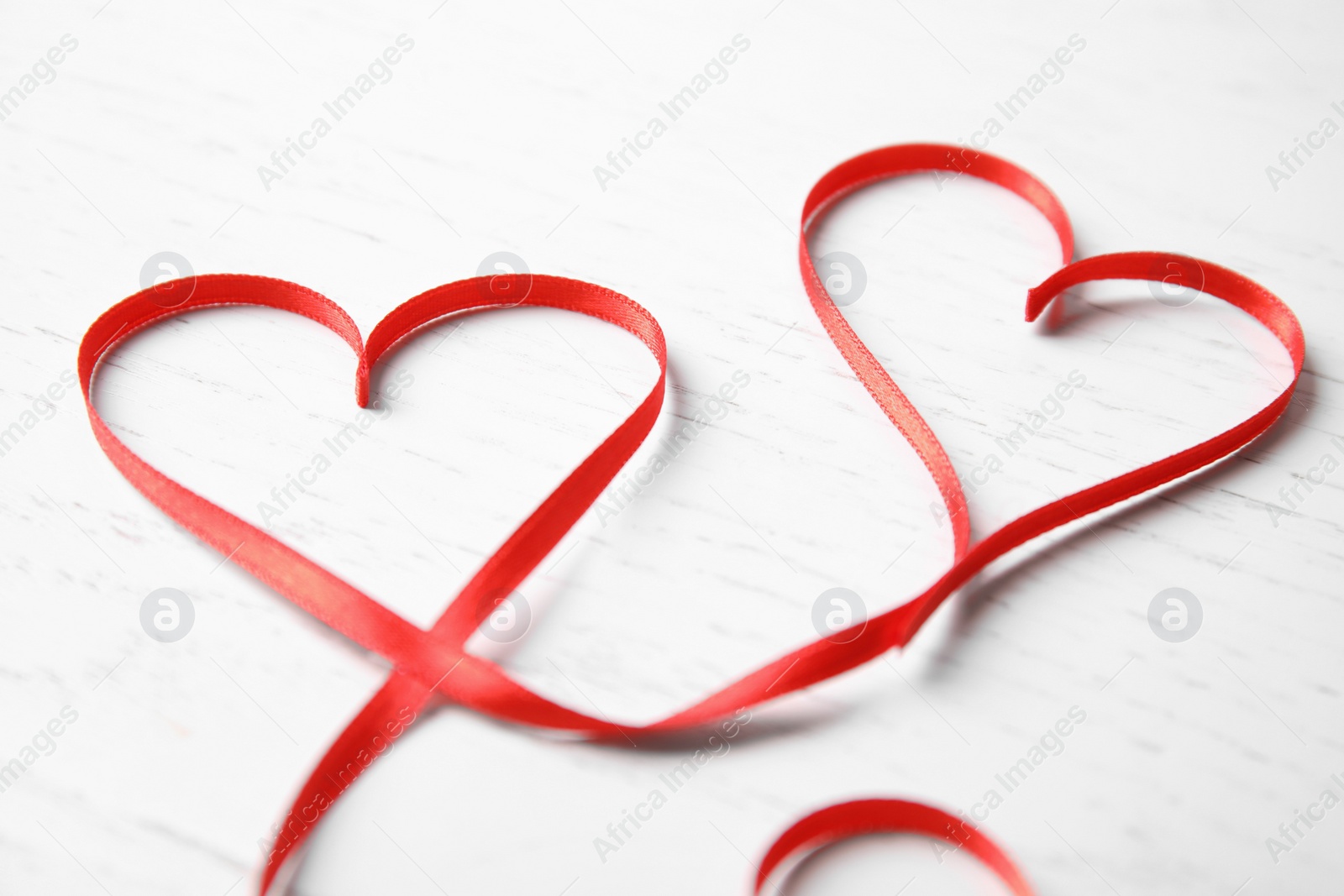 Photo of Hearts made of red ribbon on white wooden background. Valentine's day celebration