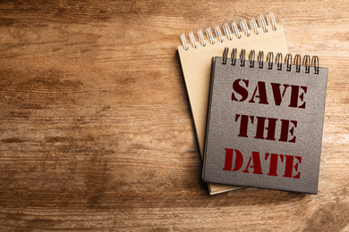 Image of Stylish notebooks with phrase SAVE THE DATE on wooden table, top view. Space for text