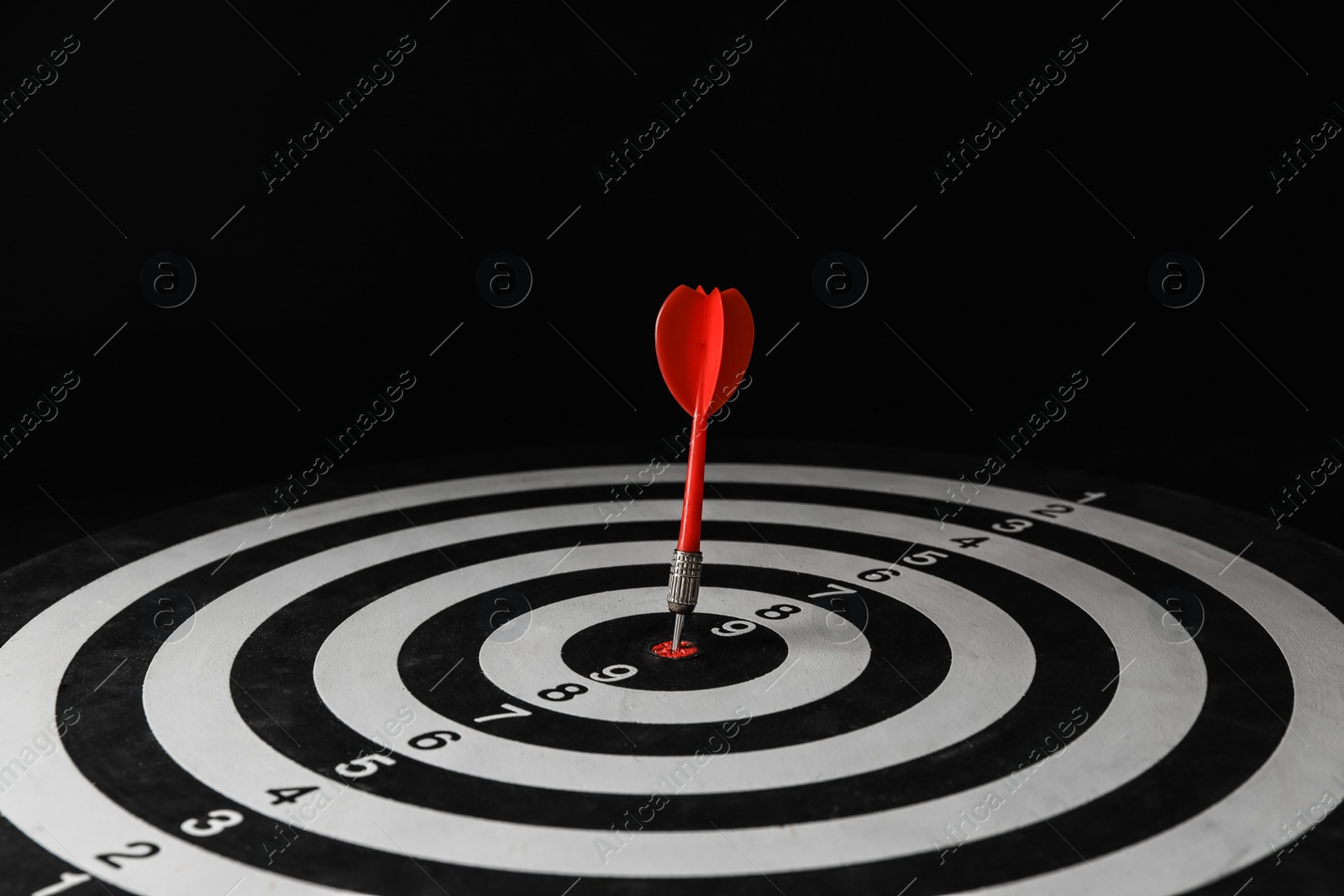 Photo of Red arrow hitting target on dart board against black background