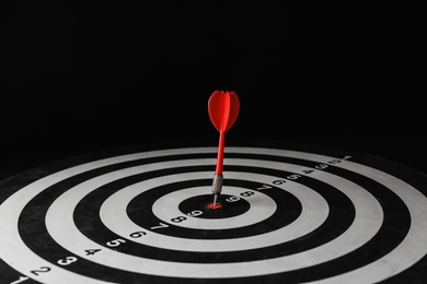 Red arrow hitting target on dart board against black background