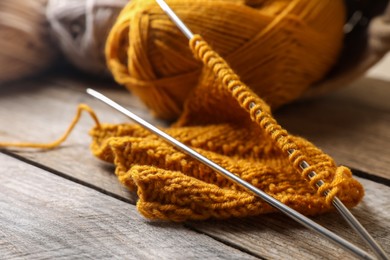 Photo of Soft orange knitting, yarns and metal needles on wooden table, closeup