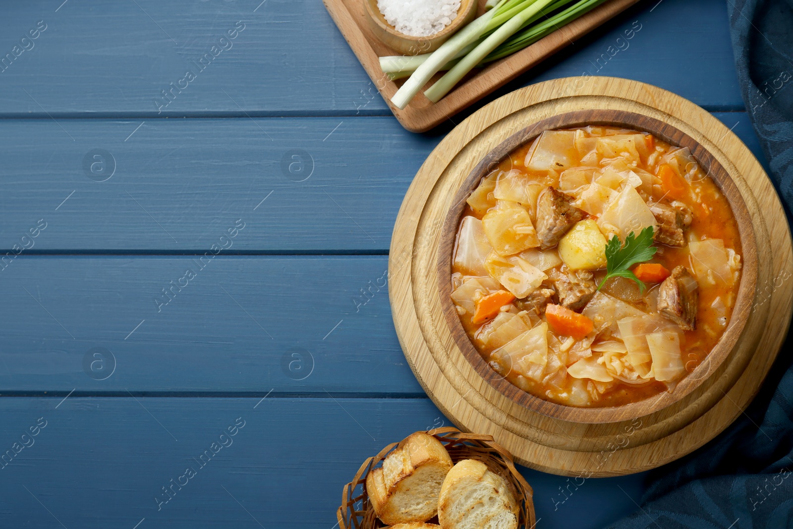 Photo of Tasty cabbage soup with meat, carrot and parsley served on blue wooden table, flat lay. Space for text