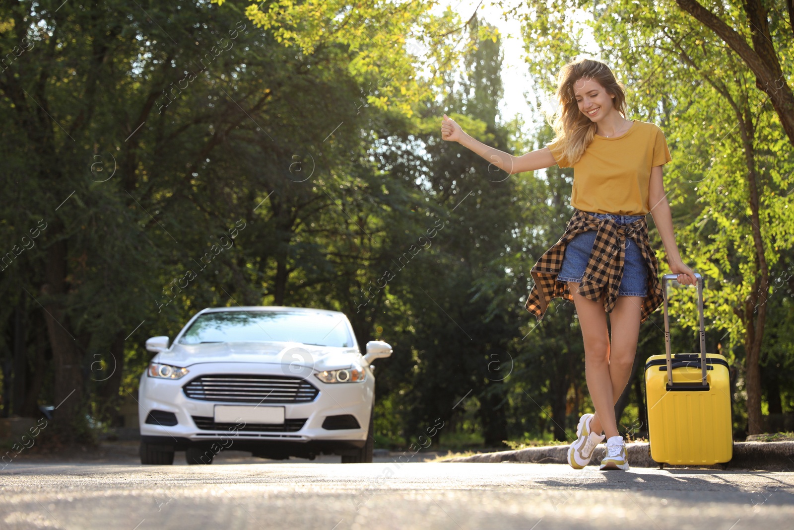 Photo of Young woman with suitcase catching taxi on city street