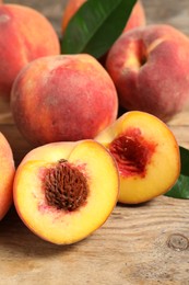 Photo of Cut and whole fresh ripe peaches with green leaves on wooden table, closeup