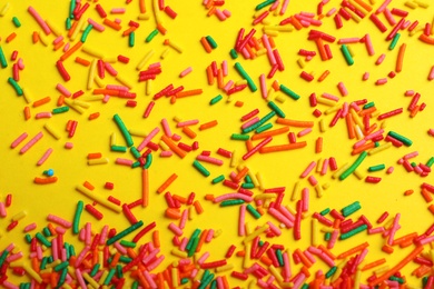 Bright colorful sprinkles on yellow background, flat lay. Confectionery decor