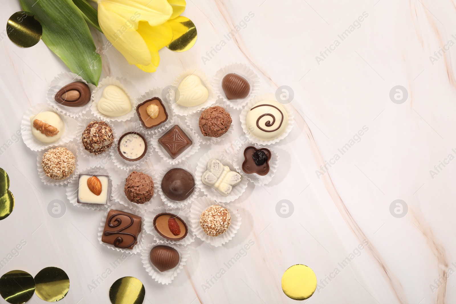 Photo of Heart made with delicious chocolate candies and beautiful tulip on beige marble table, flat lay. Space for text