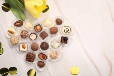 Photo of Heart made with delicious chocolate candies and beautiful tulip on beige marble table, flat lay. Space for text