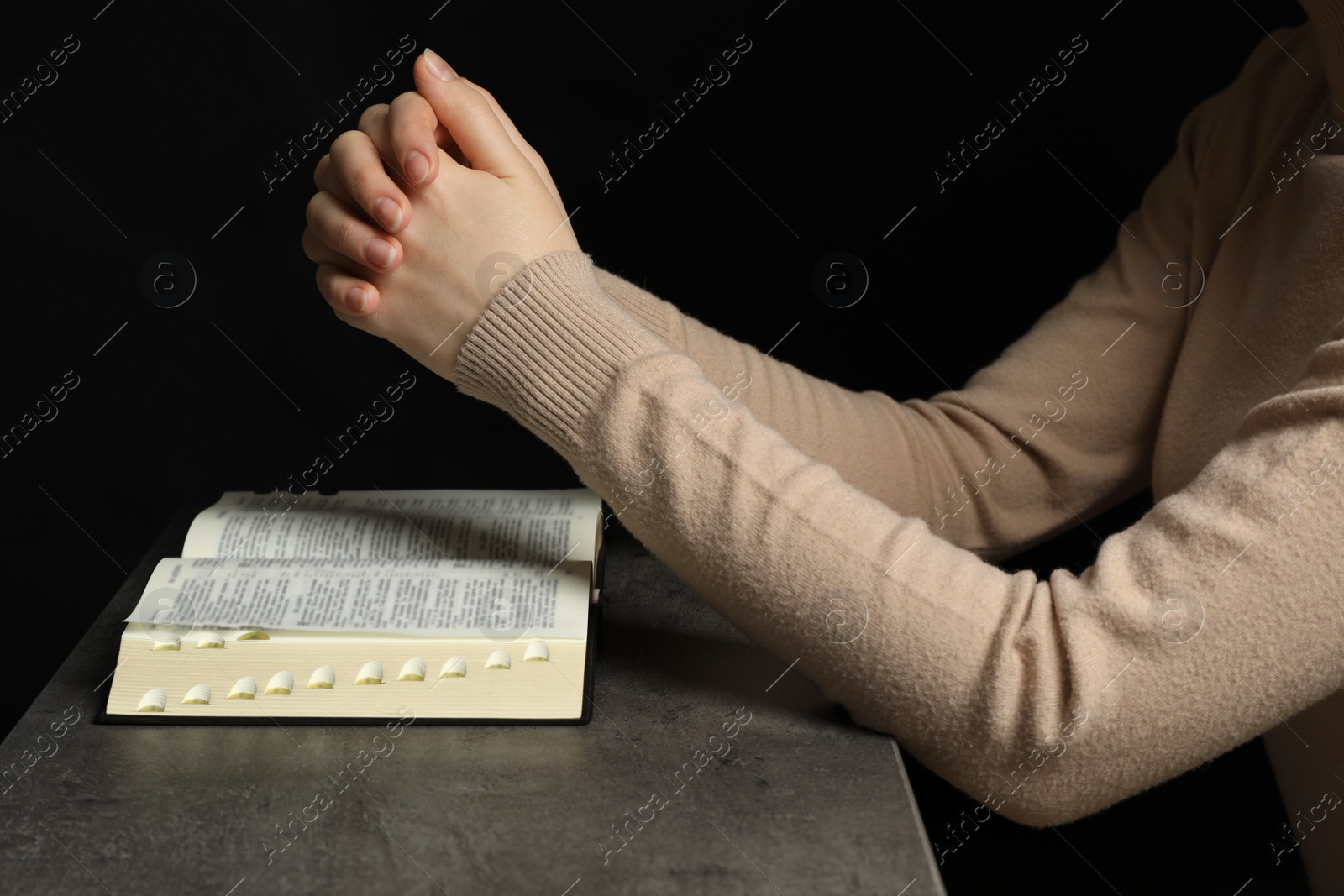 Photo of Woman praying over Bible at grey table, closeup