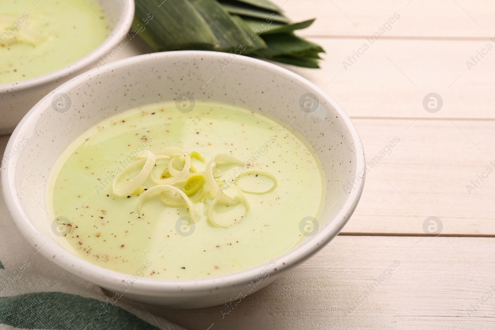 Photo of Bowl of tasty leek soup on white wooden table, closeup. Space for text