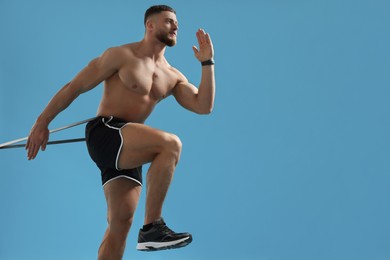 Photo of Muscular man exercising with elastic resistance band on light blue background. Space for text