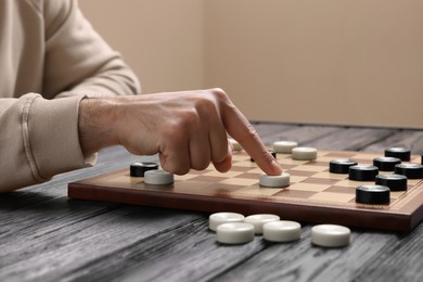 Photo of Playing checkers. Man thinking about next move at wooden table indoors, closeup