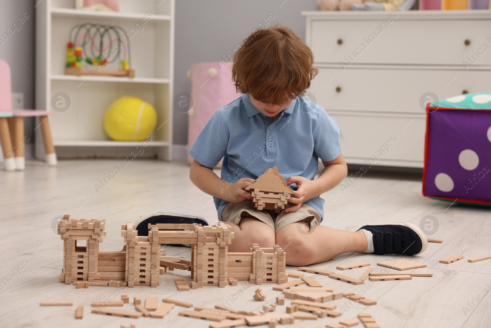 Photo of Little boy playing with wooden construction set on floor in room. Child's toy