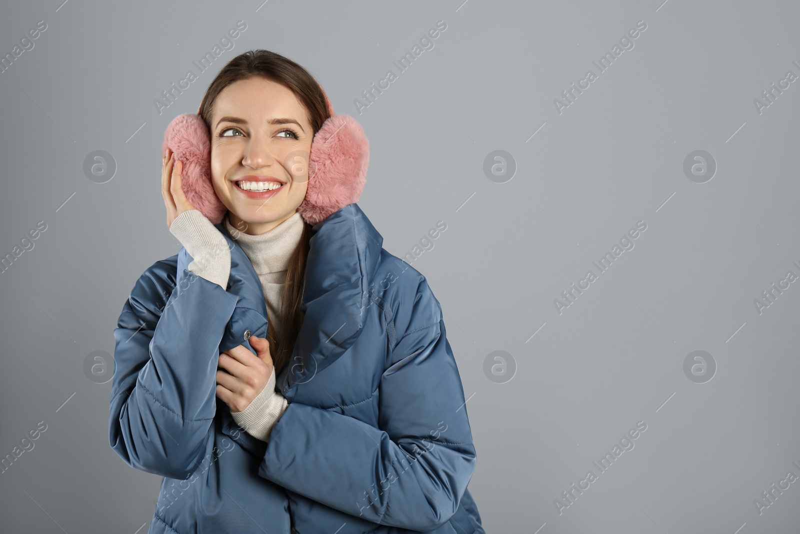 Photo of Happy woman wearing warm earmuffs on grey background, space for text