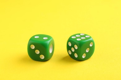 Two green game dices on yellow background, closeup