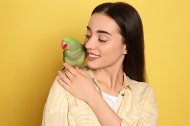 Young woman with Alexandrine parakeet on yellow background. Cute pet