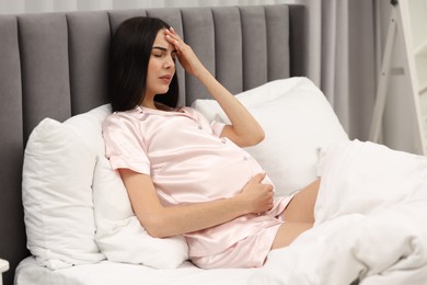 Photo of Pregnant woman suffering from headache on bed at home