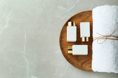 Photo of Top view of wooden tray with cosmetic bottles and towel on light grey marble table, space for text. Spa treatment