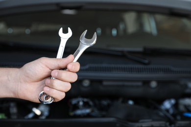 Photo of Professional auto mechanic holding wrenches near modern car in service center, closeup of hand
