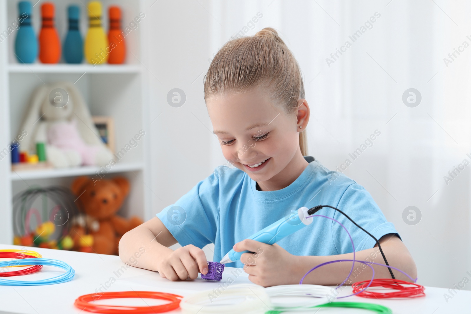 Photo of Girl drawing with stylish 3D pen at white table indoors