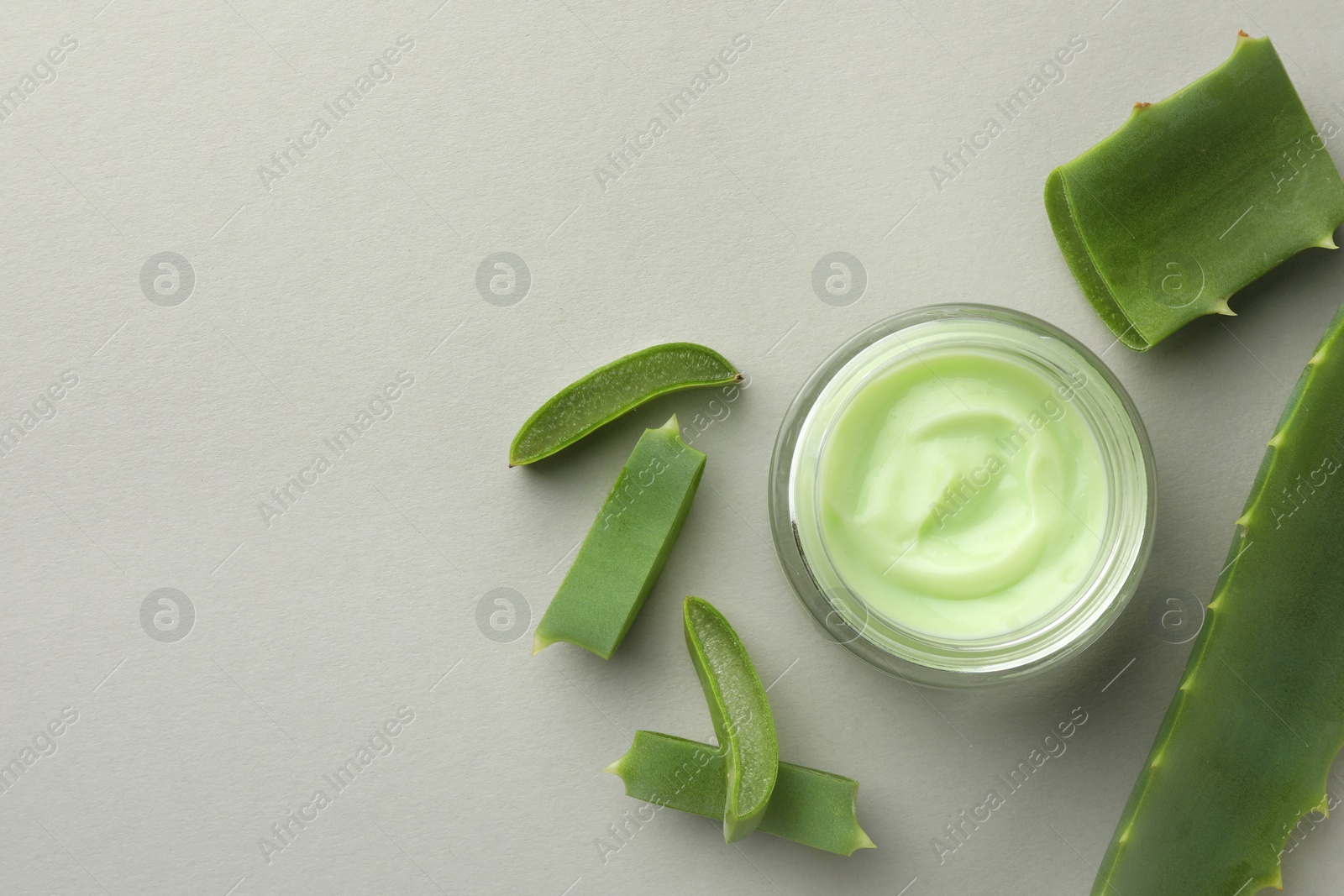 Photo of Jar with cream and cut aloe leaves on light grey background, flat lay. Space for text