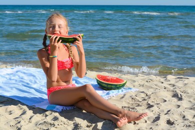 Photo of Cute little girl eating juicy watermelon on beach, space for text