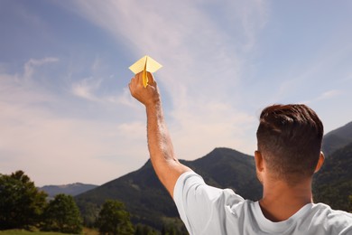 Man throwing paper plane in mountains on sunny day. Space for text