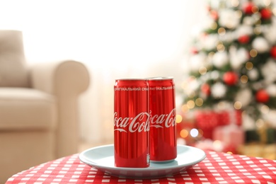 Photo of MYKOLAIV, UKRAINE - JANUARY 15, 2021: Coca-Cola cans on table in room with Christmas tree