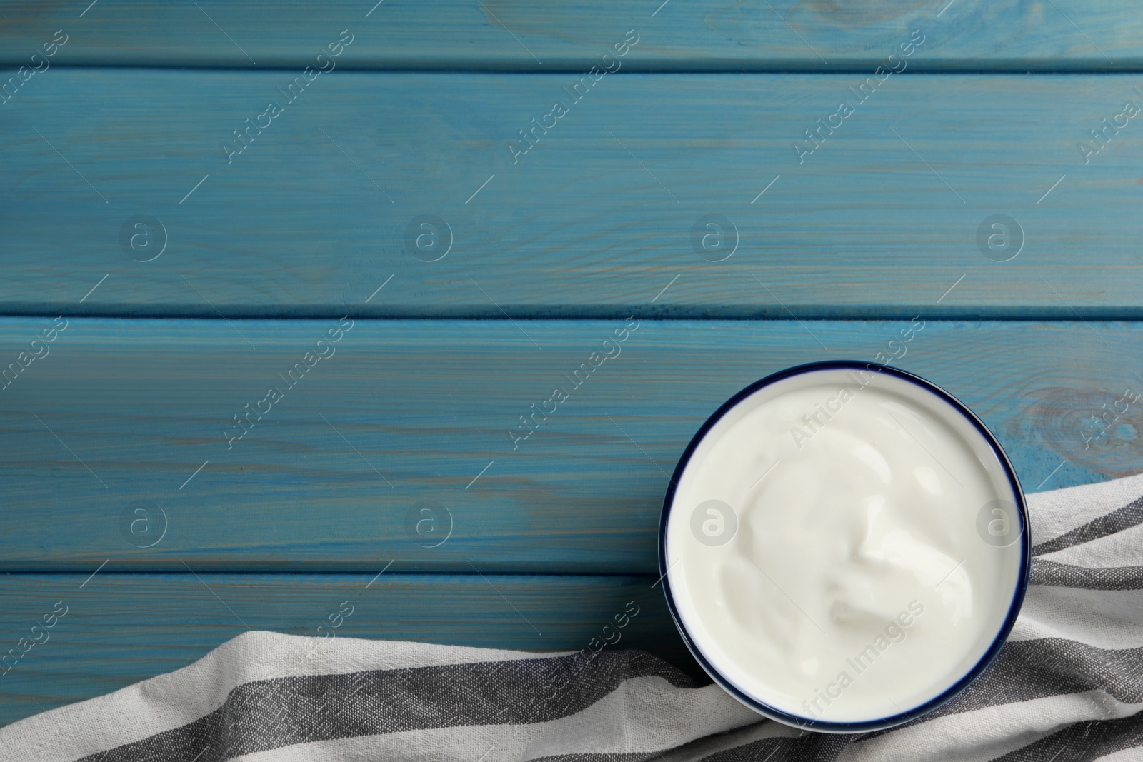 Photo of Bowl of tasty yogurt on light blue wooden table, top view. Space for text