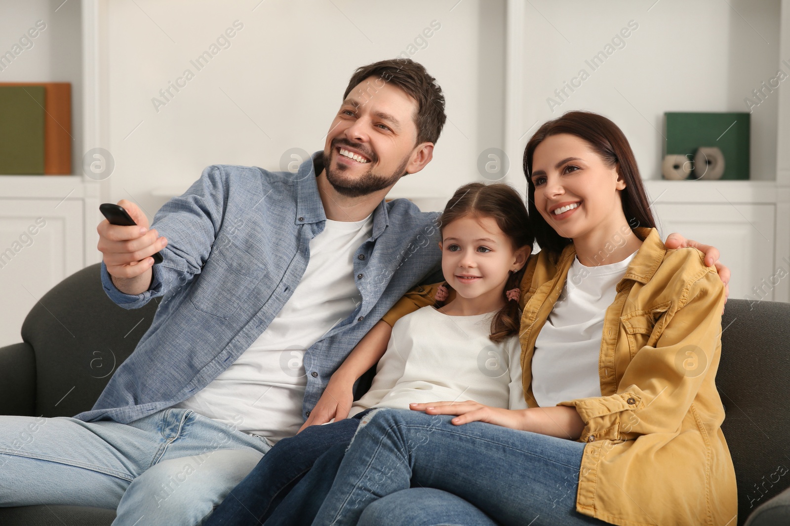 Photo of Happy family watching movie at home. Father changing TV channels with remote control