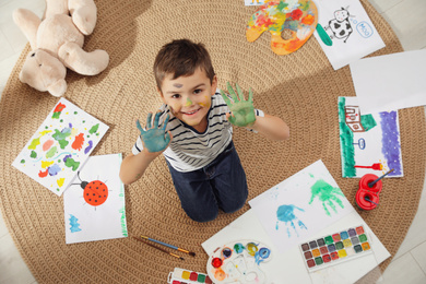 Photo of Little child with paint on face and palms in room, top view