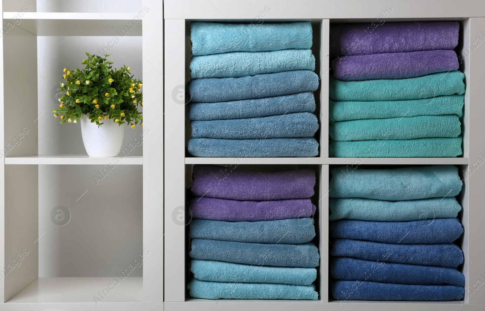 Photo of Colorful towels and houseplant on shelves. Bathroom supplies