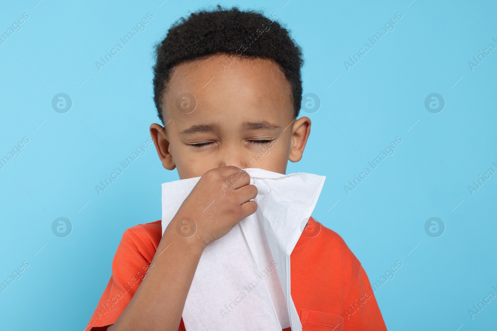 Photo of African-American boy blowing nose in tissue on turquoise background. Cold symptoms