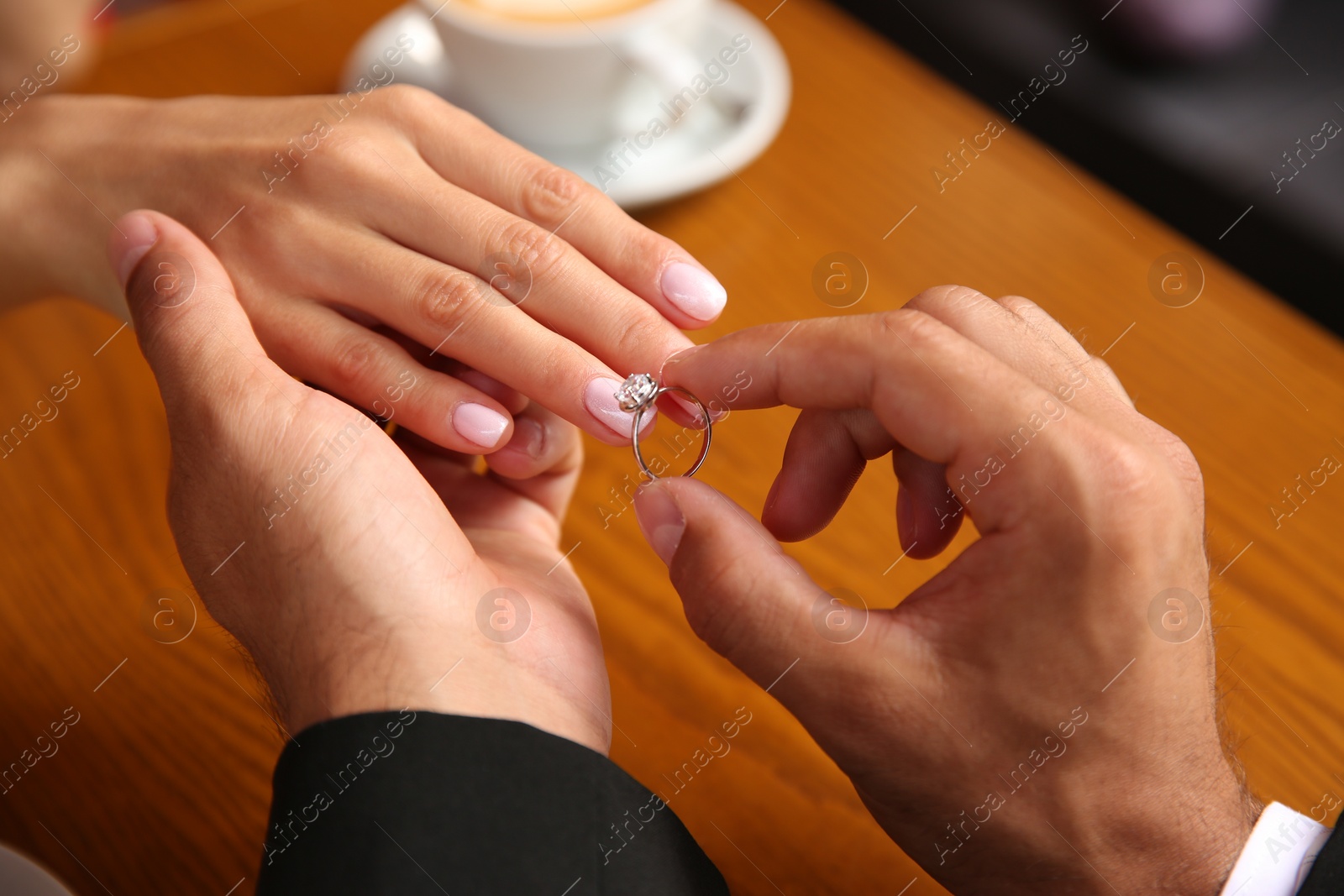 Photo of Man putting engagement ring on his girlfriend's finger in cafe, closeup