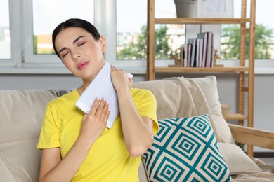 Young woman using heating pad on neck at home
