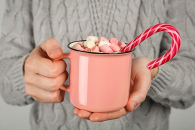 Photo of Woman holding cup of delicious hot chocolate with marshmallows and candy cane, closeup