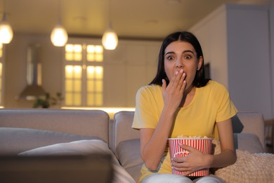 Photo of Young woman watching movie with popcorn on sofa at night, space for text