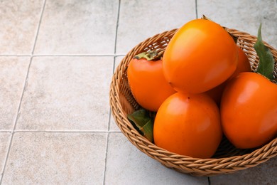 Photo of Delicious ripe juicy persimmons in wicker basket on tiled surface, space for text